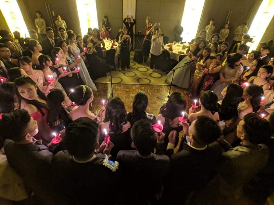 Students in formal dress holding lit candles in a circle during the junior-senior promenade.